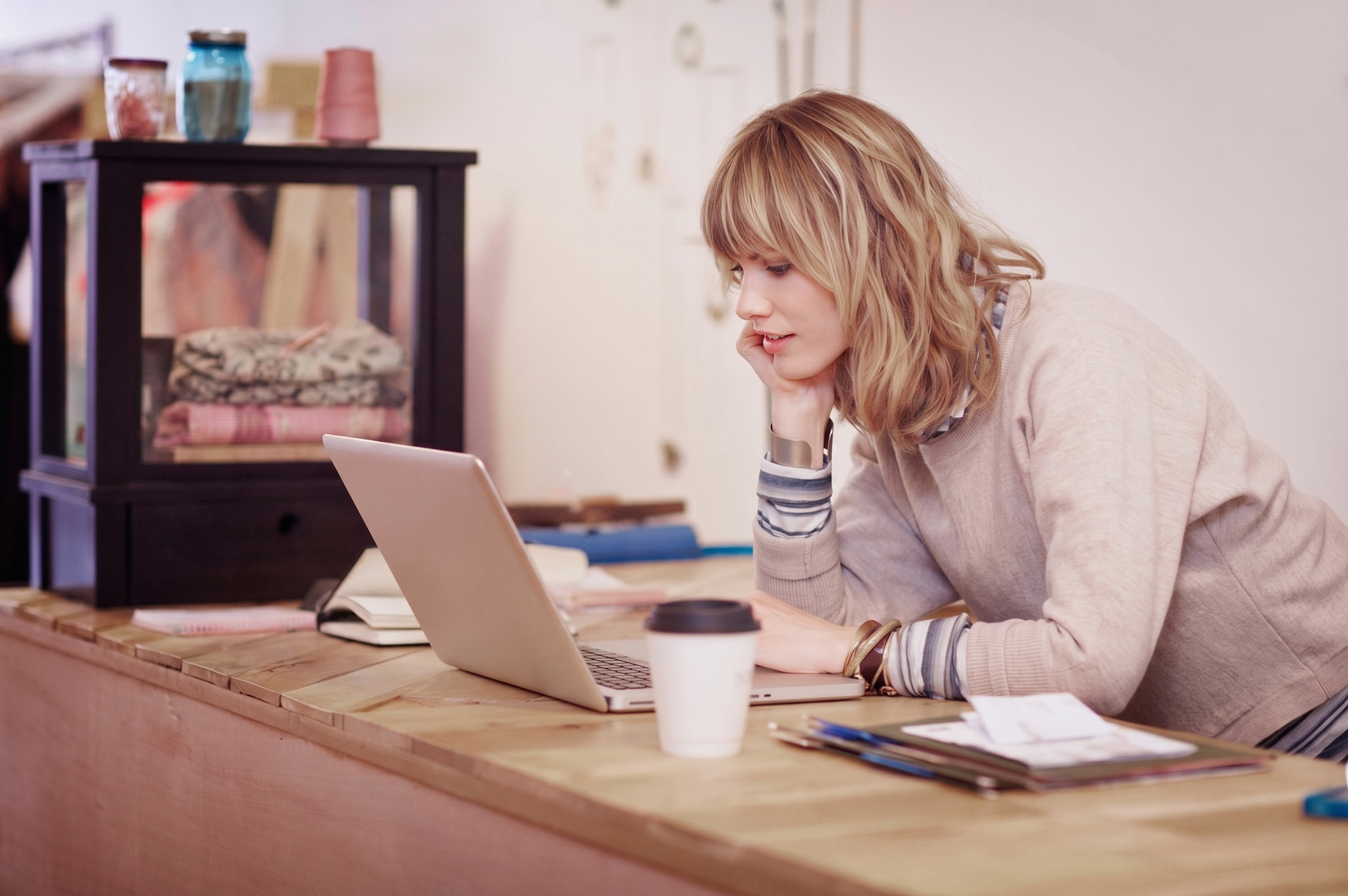 woman-leaning-on-a-counter-and-looking-at-a-laptop Homeowner reviewing checking account on mobile device